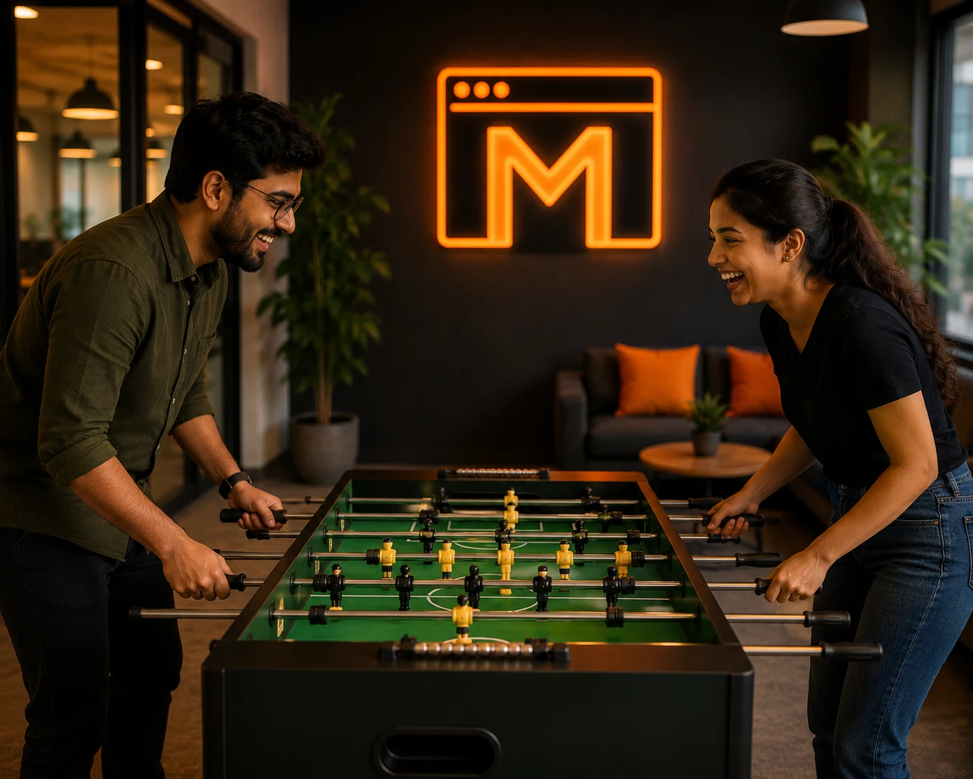 Two Mejona colleagues playing foosball and laughing, with a glowing orange Mejona M neon sign on the back wall of the recreation lounge.
